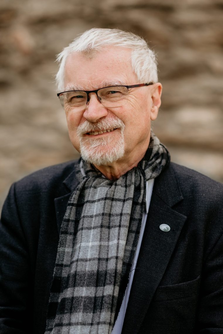 Tamás Fejérdy portréja, szürke sállal és szemüveggel