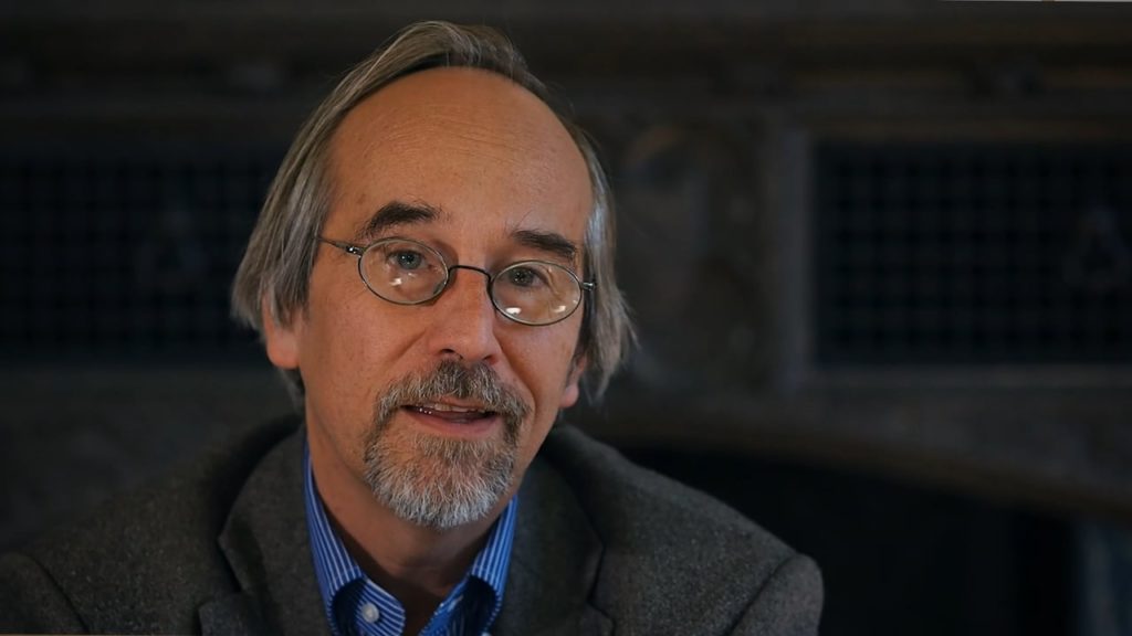 Szathmáry Eörs portréja szemüveggel, szakállal, egy szürke kabátban.