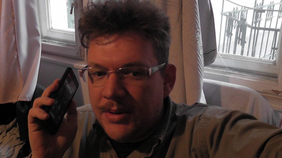 Raoul Weiss telefonál szemüvegben, háttérben ablakkal.