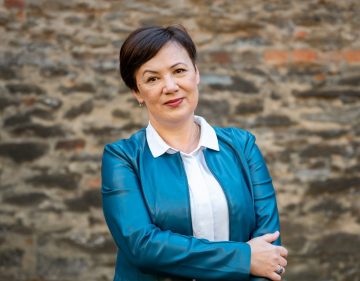 Aurélia Sőbér portréja kék blézerben, mosolyogva a kamerába.