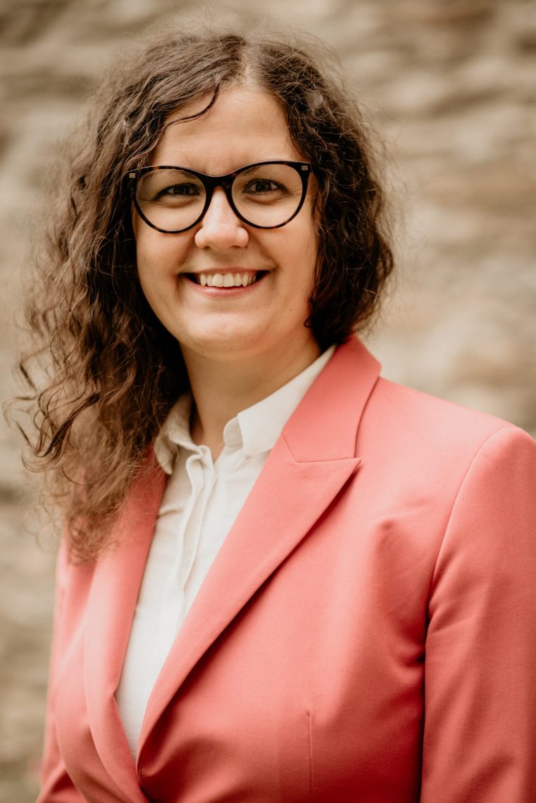 Portré Mariann Szabóról, mosolyogva rózsaszín blézerben és szemüvegben.