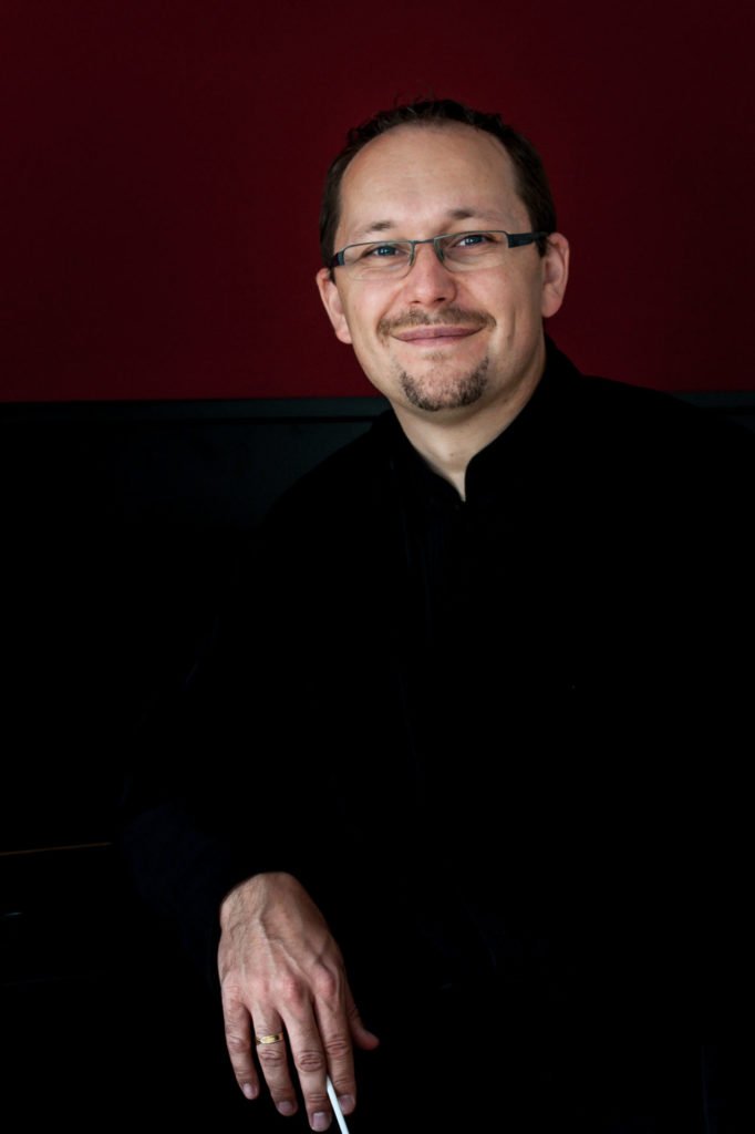 Scheer Uwe portréja szemüveggel, vörös háttérrel.