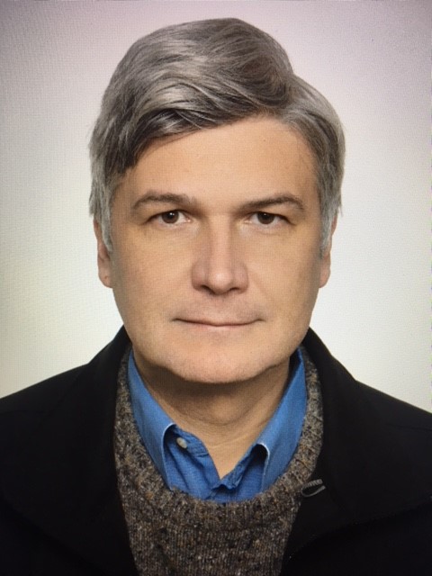 Rafal Smoczynski portréja, szürke hajú, kék ingben és fekete kabátban