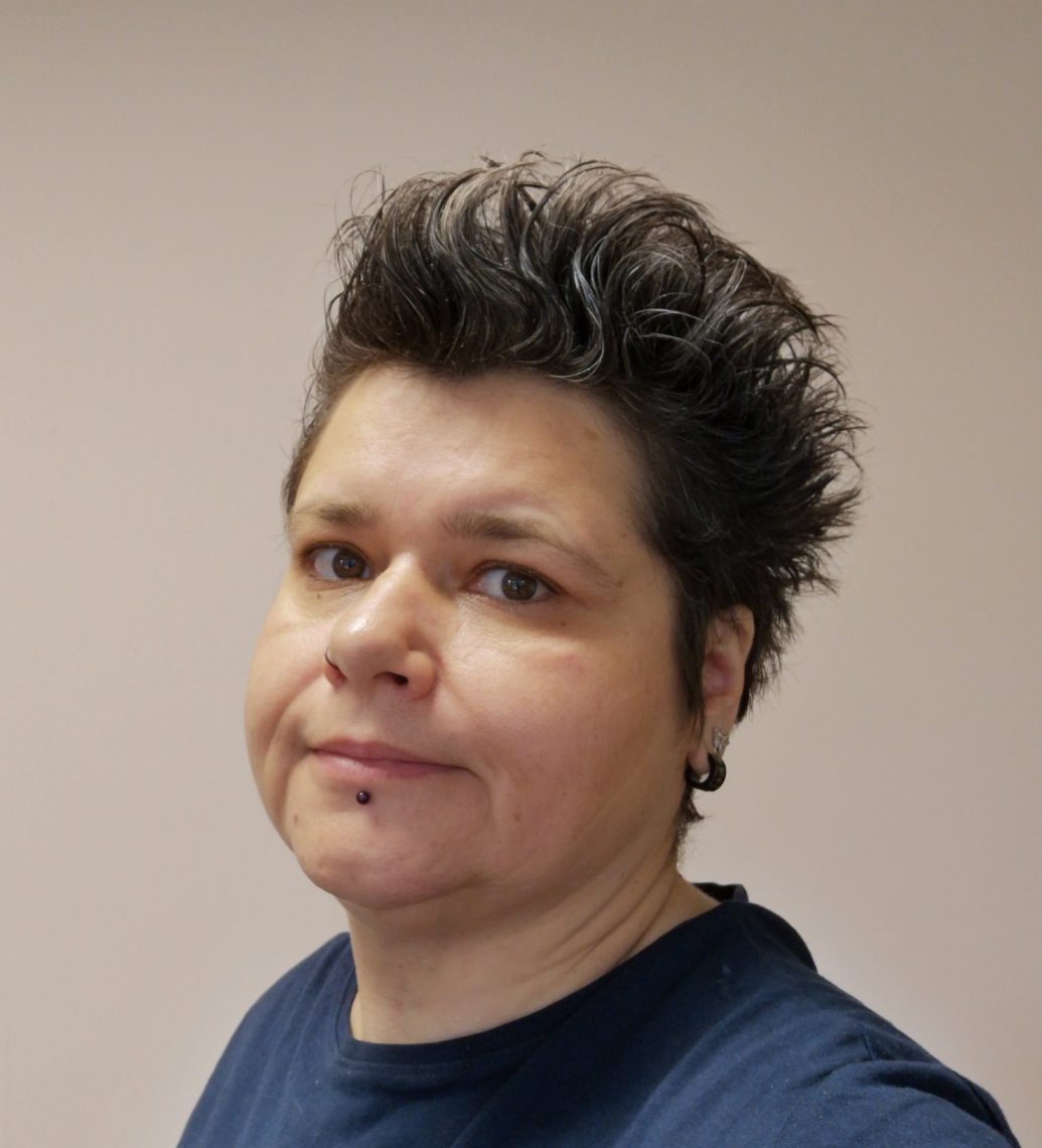 Katalin Monostori portréja rövid, szürke hajjal, piercinggel.