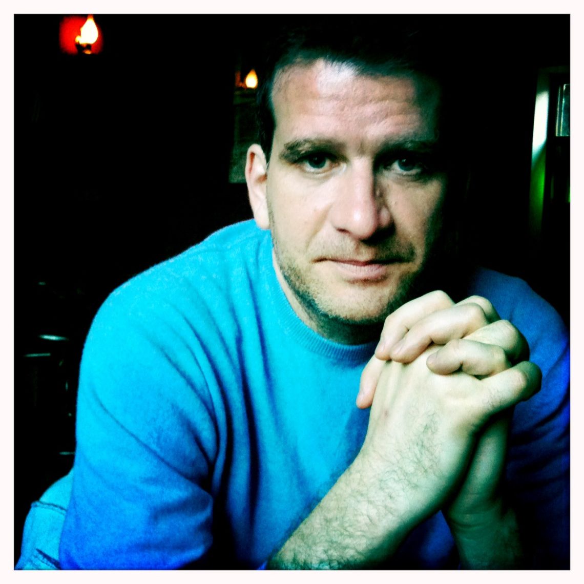 Attila Szigeti portréja kék pulóverben, összekulcsolt kézzel.