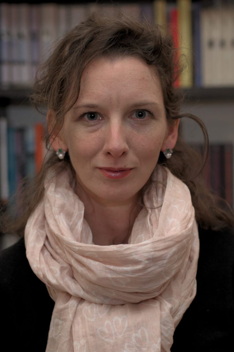 Anna Varga-Jani portréja rózsaszín sállal, könyvespolc háttérrel.