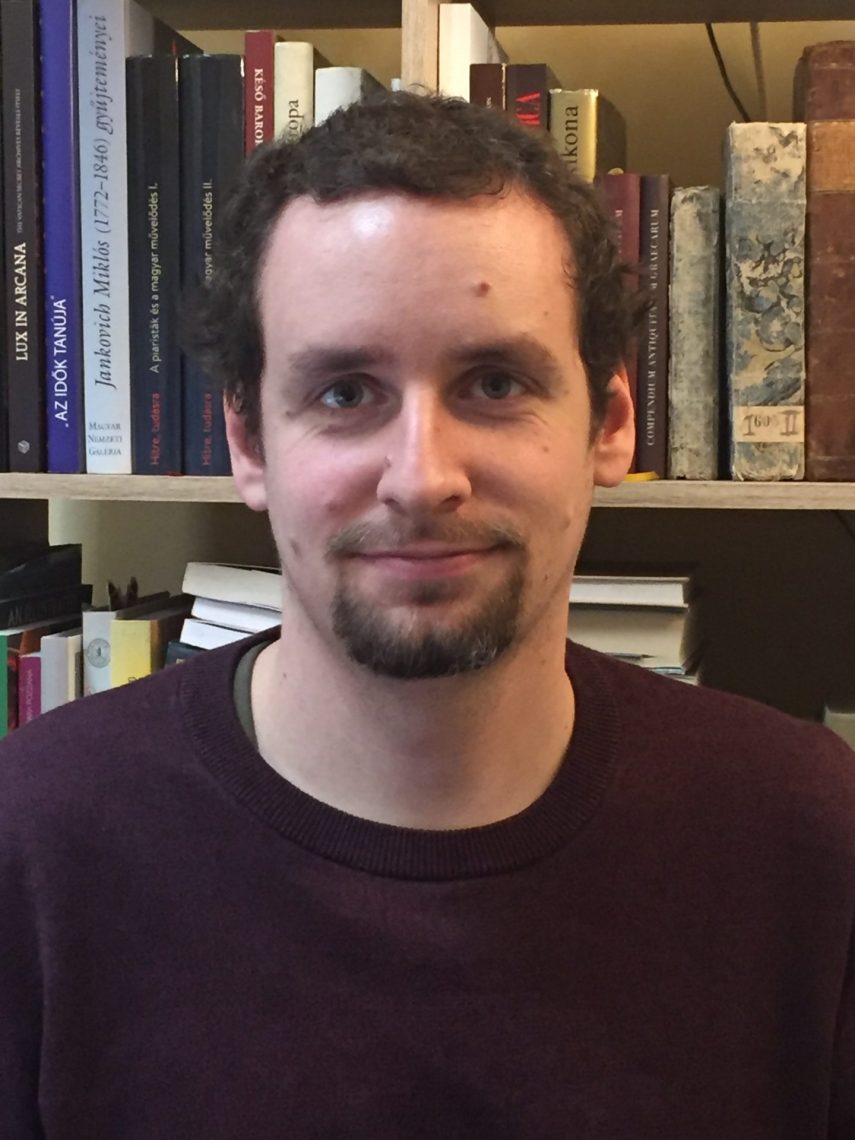 Balázs Tangl portréja, könyvespolc előtt állva.