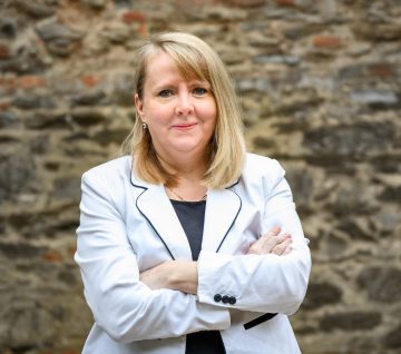 Módosné dr. Farkas Rita portréja fehér blézerben, karba tett kézzel.