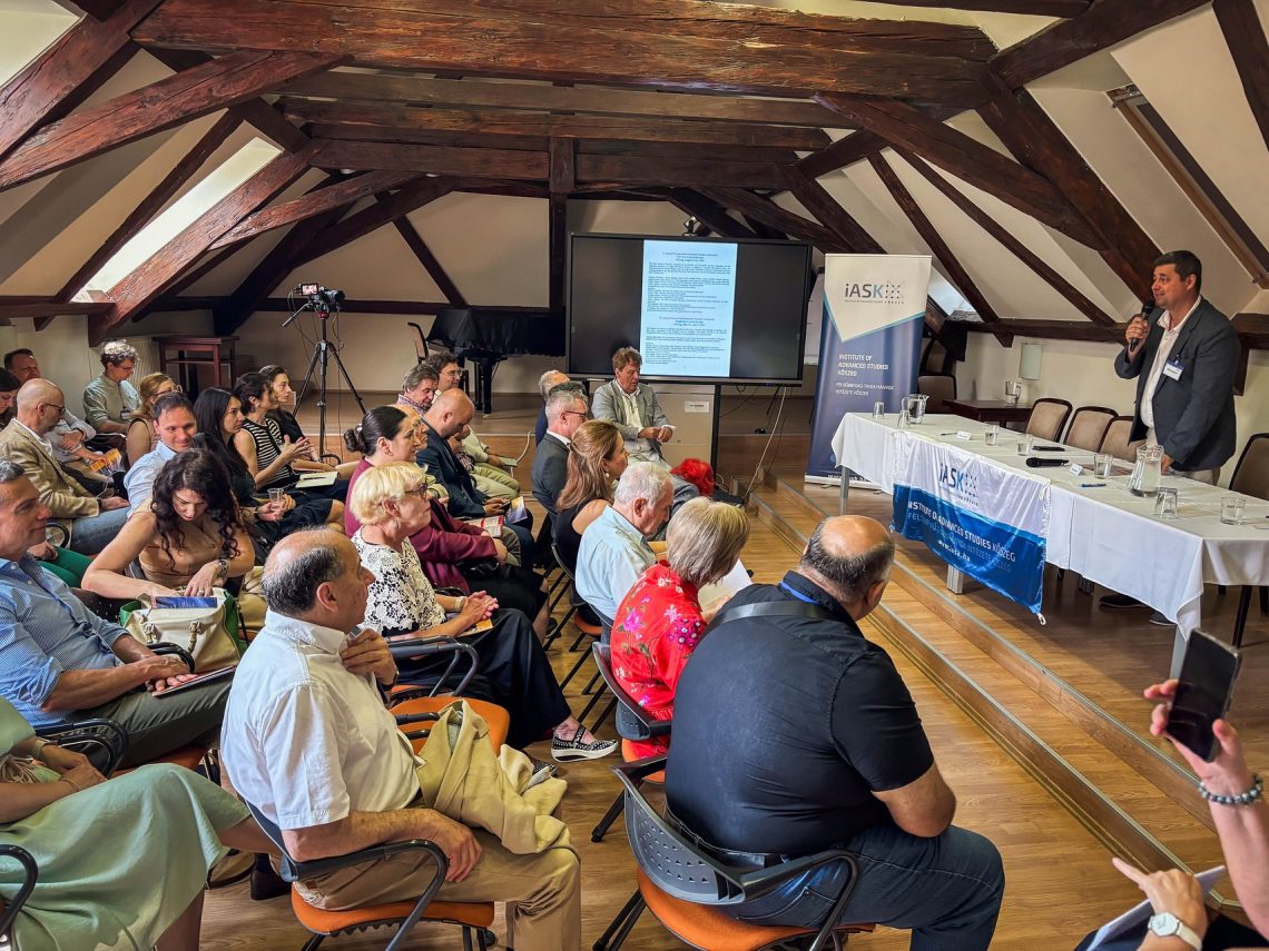 Előadó beszél a Kőszegi Nemzetközi Nyári Egyetemen, hallgatóság a teremben. ASK logo.