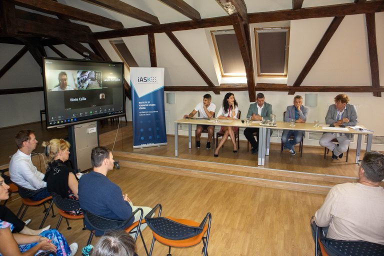 Panelbeszélgetés az IASK-ban, kivetítőn online résztvevőkkel. IASK logo látható.