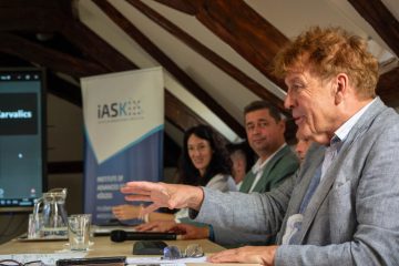 Előadó gesztikulál egy konferencián Kőszegen. iASK látható a háttérben.