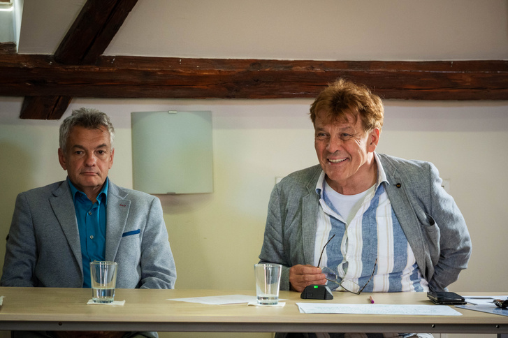 Két férfi ül egy asztalnál, egy komoly, egy mosolygós. Valami történik ebben a kis magyar városban.