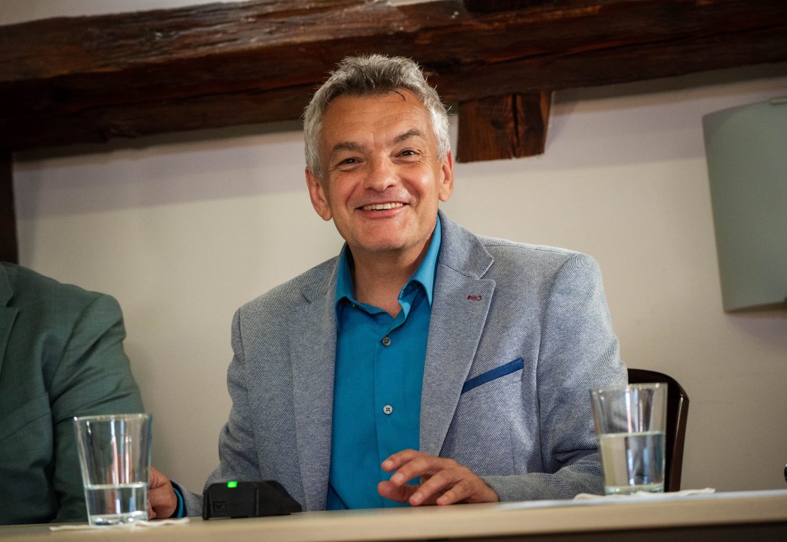 Novák Tamás portréja, mosolyogva az asztalnál.