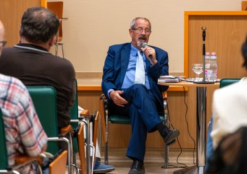 Kék öltönyös férfi könyvbemutatón beszél