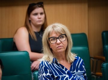 Balázs Edit a "Csillogás és katasztrófa" könyvbemutatóján, kék-fehér mintás ingben.