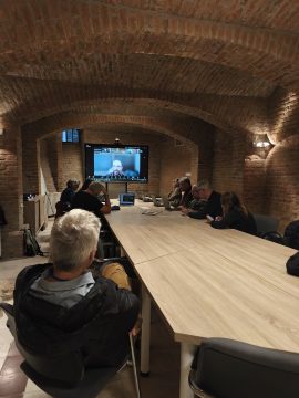 A résztvevők konferenciaasztalnál nézik a virtuális előadást