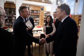 Két férfi kezet fog Kőszegen, a háttérben könyvespolcok és más emberek láthatók.