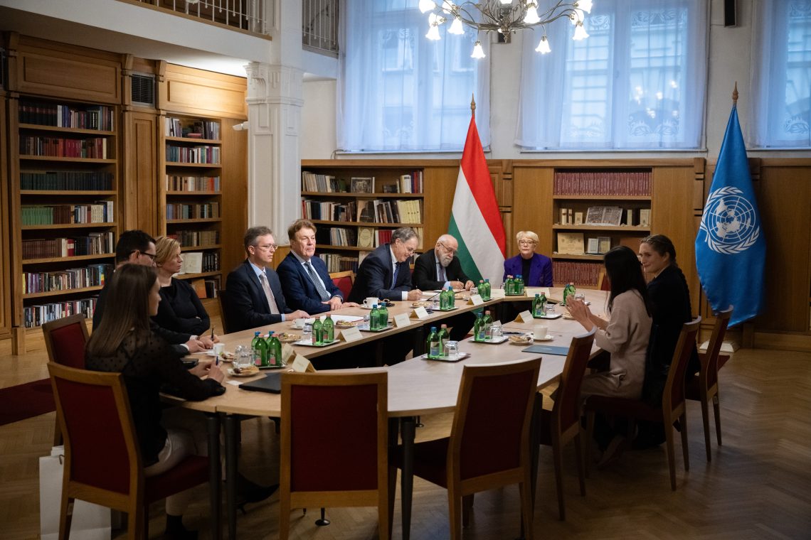 Tisztviselők találkoznak magyar és ENSZ-zászlókkal egy könyvtári környezetben.