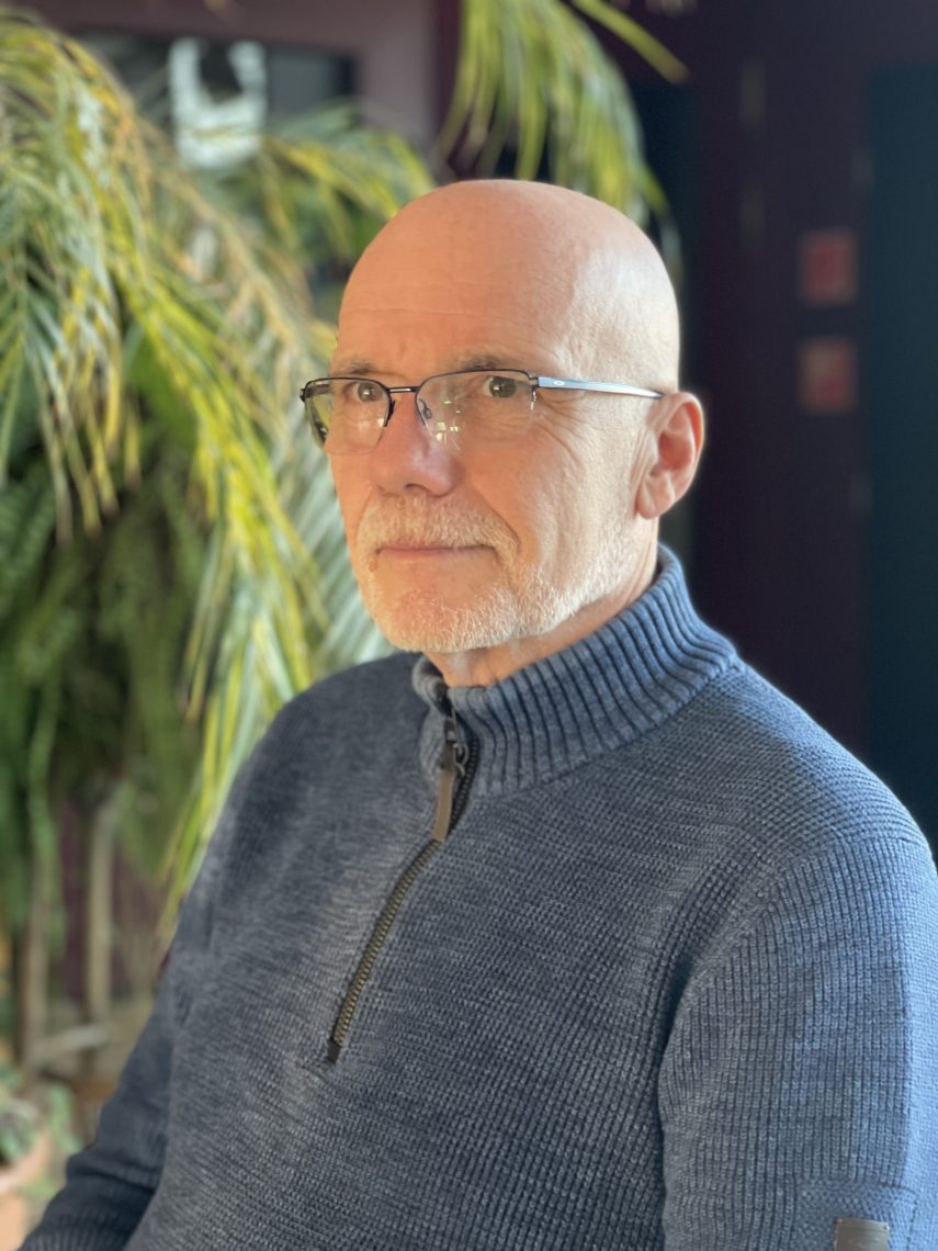 András Nyírő portréja szemüveggel és kék pulóverben, növényekkel a háttérben.