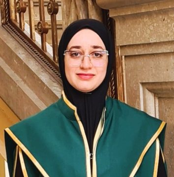 Feyrouz Ahlam Saidi fejkendőben, szemüvegben, zöld talárban.