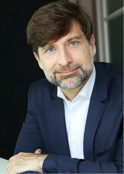 István Peták portréja: mosolygó, szakállas férfi kék zakóban.